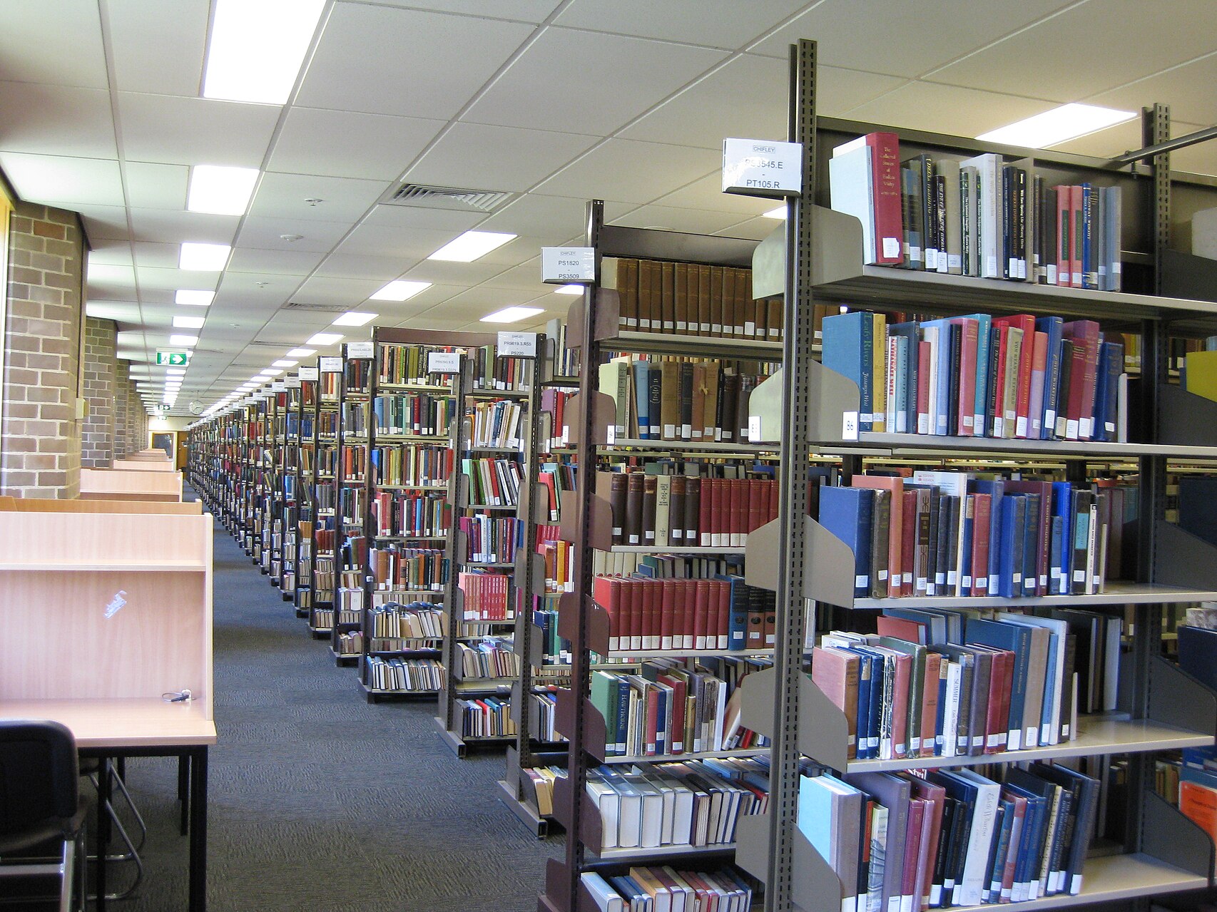 A corridor through the library, with row after row of metal bookshelves on the right, and desks for private study on the left