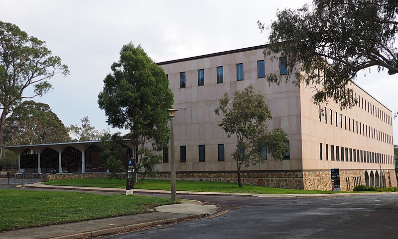 Menzies Library: a large, boxy building, with smooth stone walls and a regular grid of windows. In front: a few trees and a driveway.