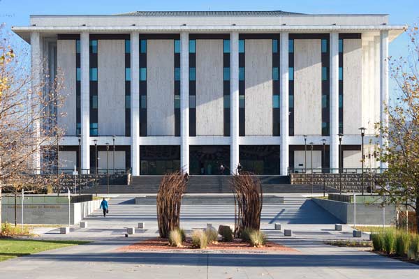 The library façade. Out front is a flowerbed with sculptural planting, and a wide staircase leading up to the building. The library is a starkly modern take on the "stripped classical," with simple vertical columns interspersed by narrow vertical windows and flat stone panels.